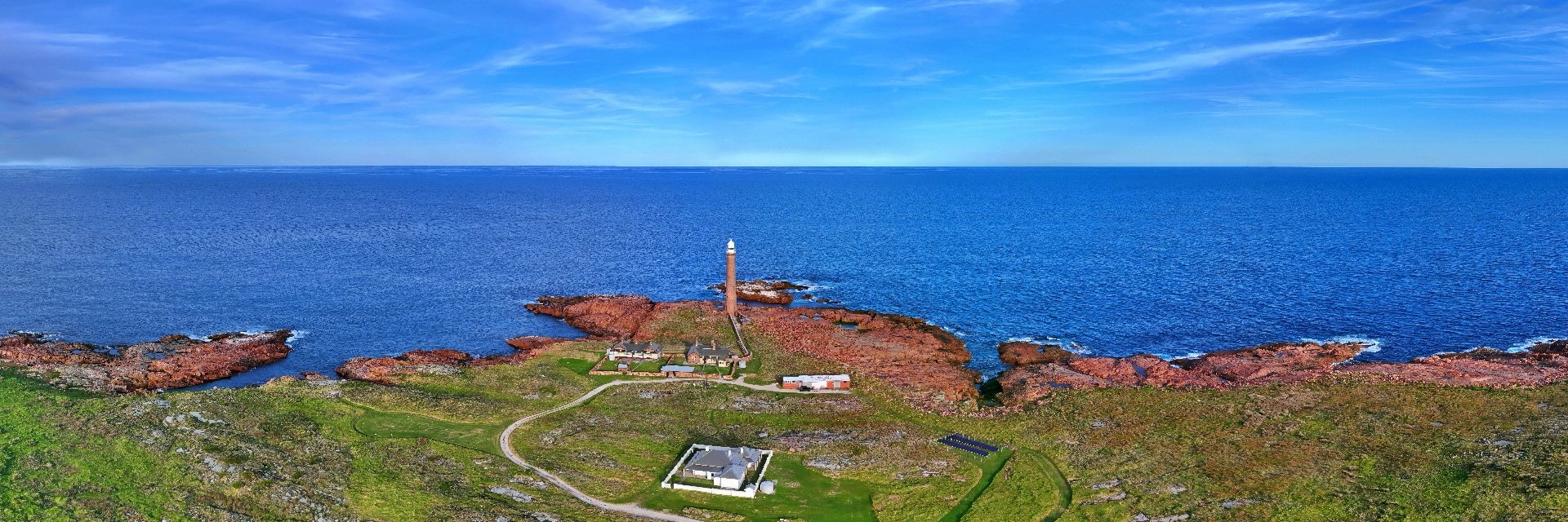 Aerial panorama of Gabo Island Lighthouse on red granite, with keepers’ cottages, solar panels and the ocean beyond.