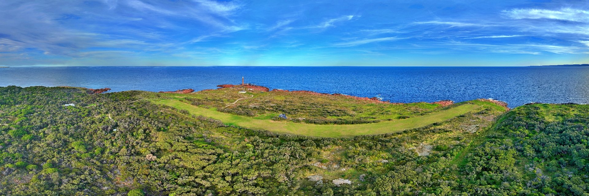 Aerial panorama of Gabo Island looking across the grass airstrip toward the lighthouse and open ocean.