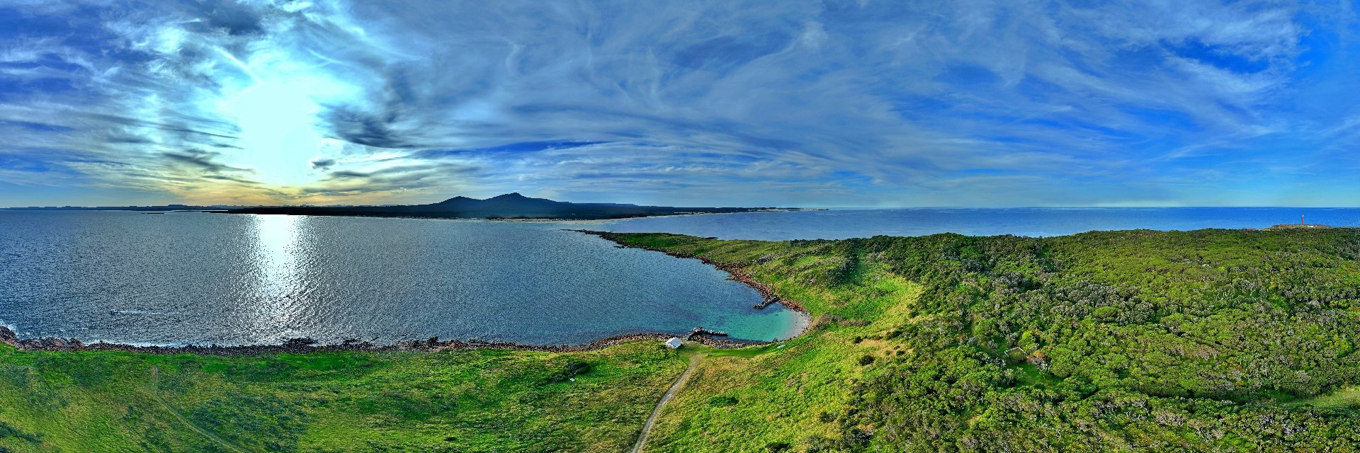 Aerial panorama from Gabo Island looking toward the Howe Ranges and East Gippsland coast, with sun on the water.